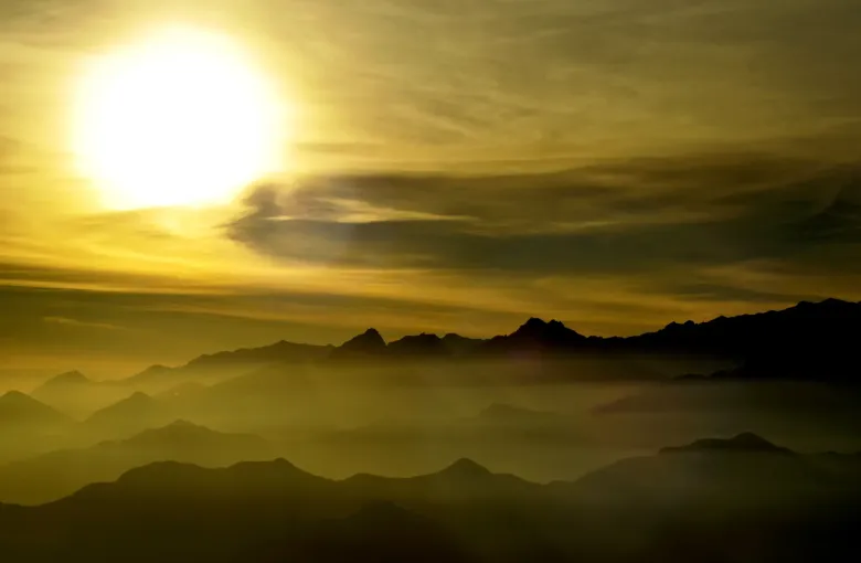 Ridge after ridge of the Sierra Nevada de Santa Marta silhouetted through cloud at sunrise, the sun high and hazy above them.