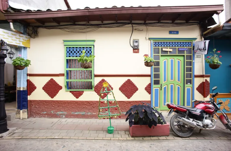 The front of a house in Guatape painted white with a red and blue patterned zocalo along its base and plants hanging by the door.