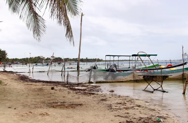 Open boats and a shaded frame pulled up on wet sand at the water's edge, under a flat overcast sky.