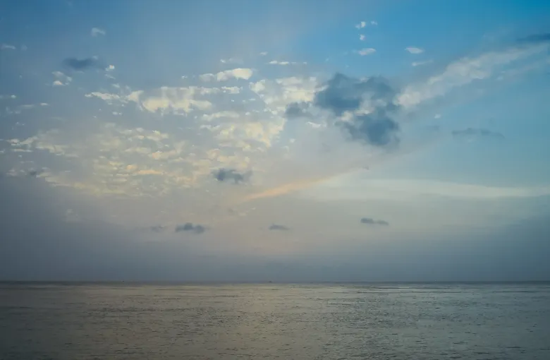 A wide, almost featureless view of pale sea meeting a hazy sky, with thin cloud low on the horizon and no land in sight.