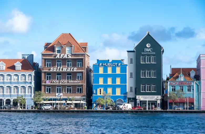 The waterfront of Willemstad in daylight, with painted colonial buildings along the quay and small craft moored in the bay.