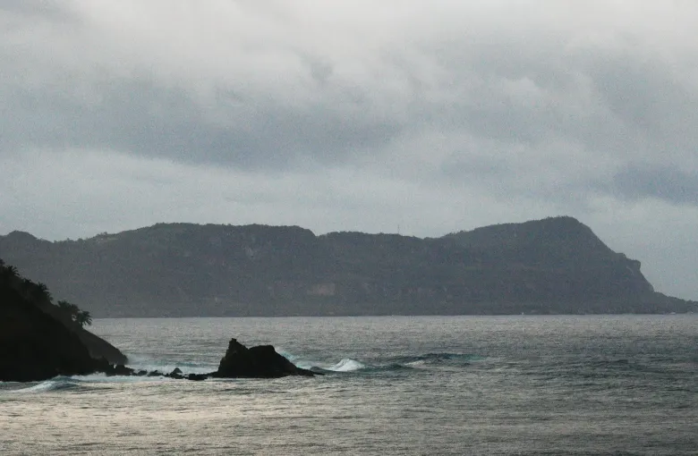 A high green headland drops to the sea at Cabo Cabron on the Samana peninsula, under an overcast sky.