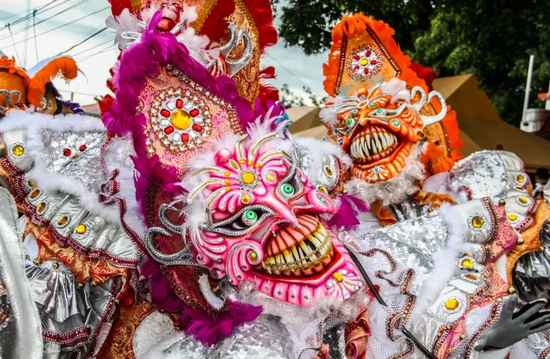 An ornate pink and white horned carnival mask with mirrored studs, worn at a Dominican carnival.