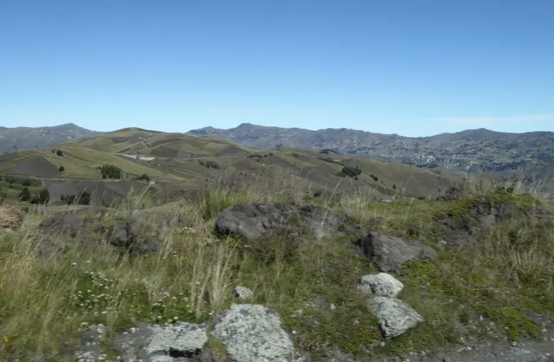Cultivated Andean hillsides in strips of green and gold falling away from a highland road under a clear sky.