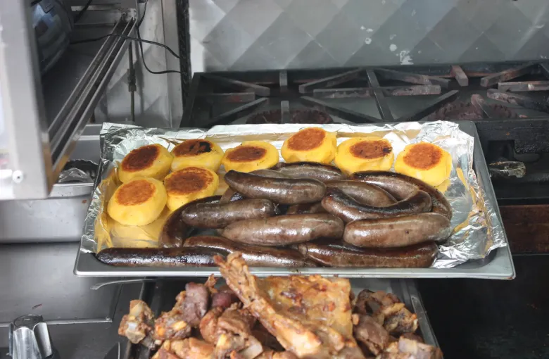 Golden llapingachos, the fried potato cakes of the Ecuadorian highlands, on a tray beside grilled chorizos.