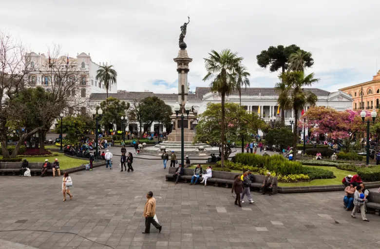 The Independence monument at the centre of Plaza Grande in Quito, with palms, gardens and the colonnaded presidential palace behind.