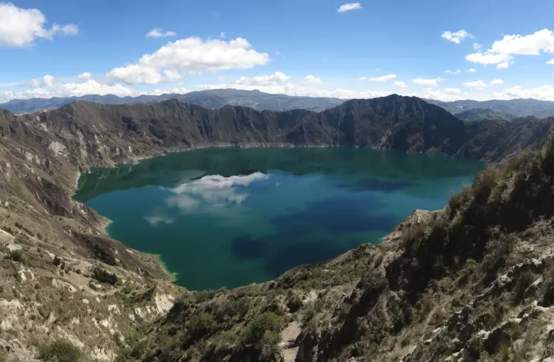 The turquoise crater lake of Quilotoa held inside steep volcanic walls, with the Andes ranged along the horizon.