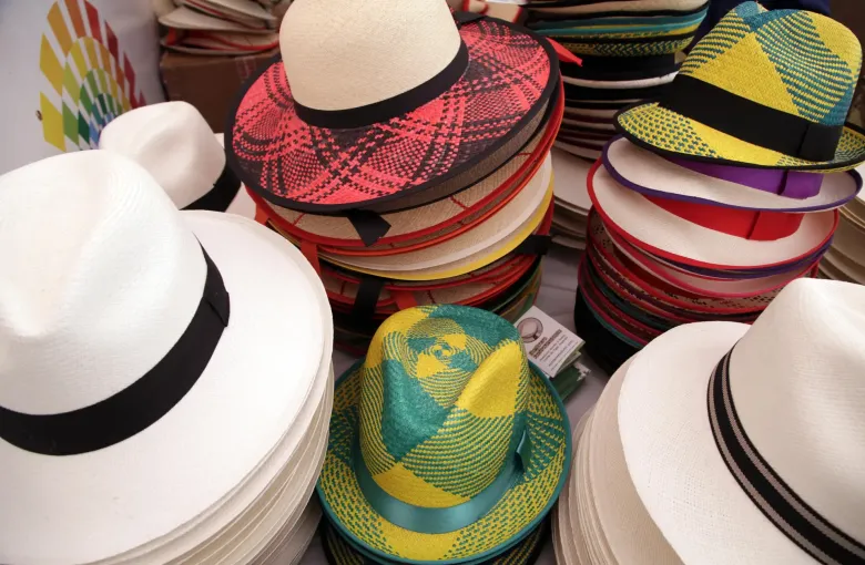 Stacks of woven toquilla straw hats, some in natural cream and others dyed in bright patterns, displayed for sale.