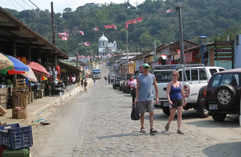 A cobbled street lined with small shops and awnings, bunting overhead and a white church tower at the far end.