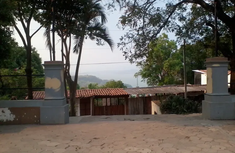 A cobbled terrace between stone gateposts, looking out over tiled roofs and trees toward distant hills.