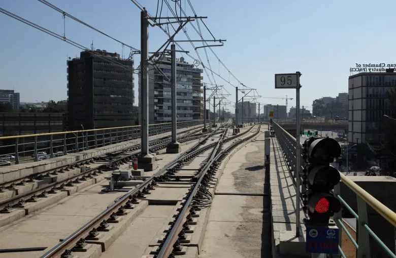 Light rail tracks running along an elevated alignment in Addis Ababa, Ethiopia, under overhead wires, with a signal in the foreground and tower blocks beyond.