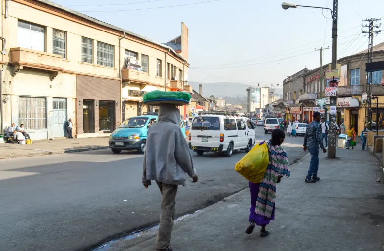 A street in central Addis Ababa, Ethiopia, lined with low shopfronts, with minibuses at the curb and people walking along the roadside.
