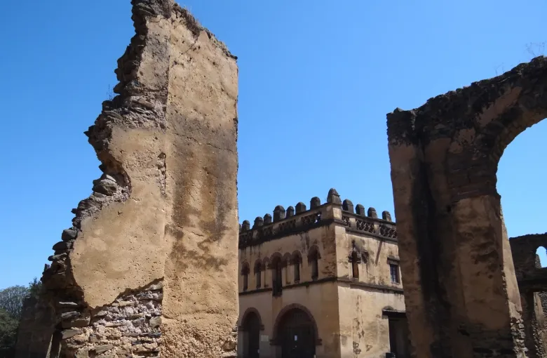 Standing stone walls and arches of the Royal Enclosure at Gondar, Ethiopia, framing a crenellated tower under a clear sky.