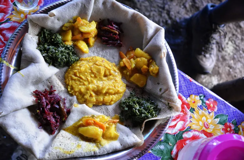 A shared platter of injera in Ethiopia topped with mounds of lentil, split pea and cooked green vegetable dishes.