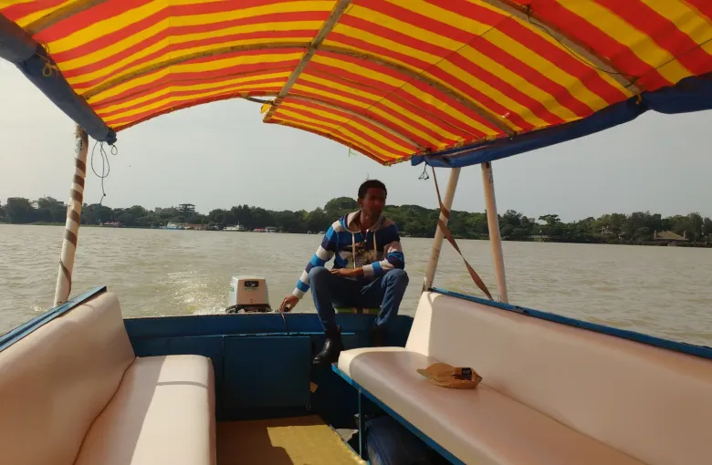 The shaded interior of a small tour boat on Lake Tana, Ethiopia, with padded bench seating under a striped awning and the wooded shoreline beyond.