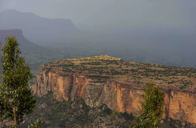 A flat-topped sandstone mesa catching low sunlight in the Tigray highlands of Ethiopia, with hazy ridges receding behind it.