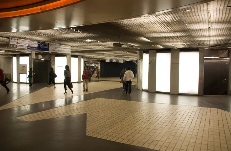 A wide underground interchange concourse in Paris with a handful of distant passengers crossing the tiled floor.