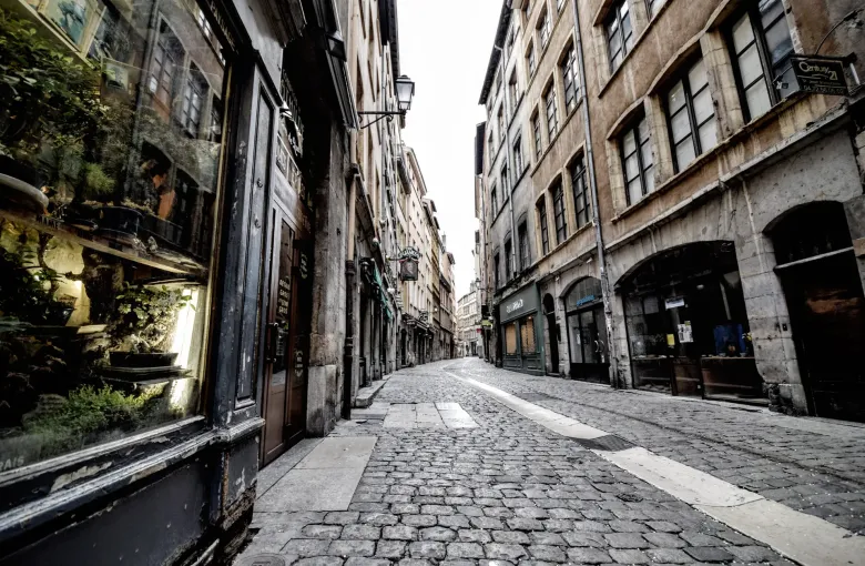 Rounded cobbles filling the foreground of a narrow street of tall shopfronts in the old quarter of Lyon, France.