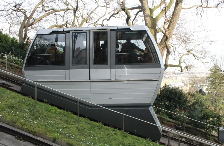 A funicular car on its short steep track up the side of the Montmartre hill in Paris, with trees on either bank.