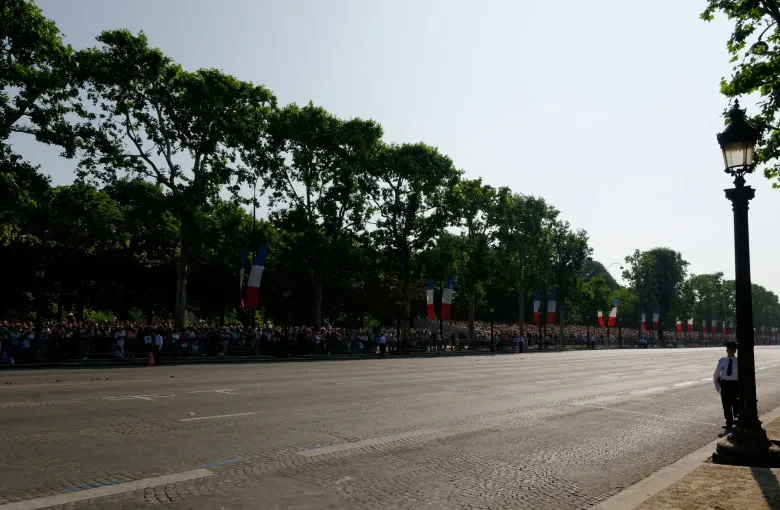 French flags hung the length of the Champs-Elysees above a crowd behind barriers on a national holiday in Paris.