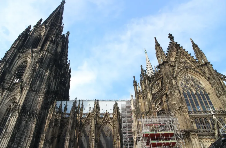 The south flank and spires of Cologne Cathedral seen from below, with restoration scaffolding standing against the stonework.