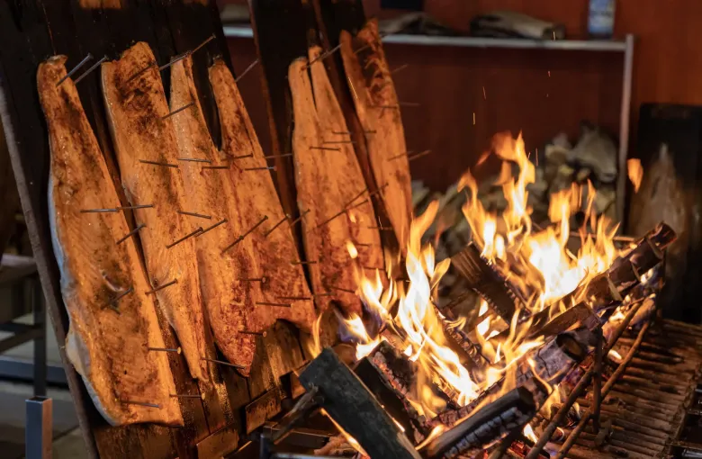 Sides of salmon nailed to wooden planks and set around an open fire to cook at a German market stall.