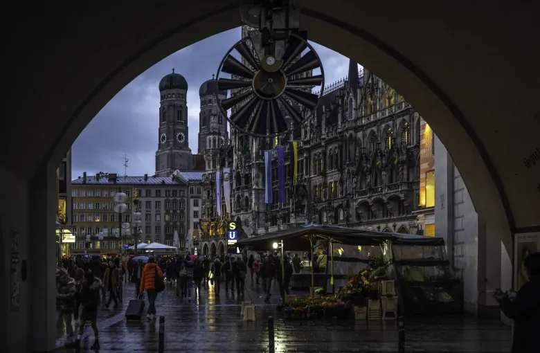 The Marienplatz in Munich seen through an archway on a wet evening, the paving reflecting the lights of the square.
