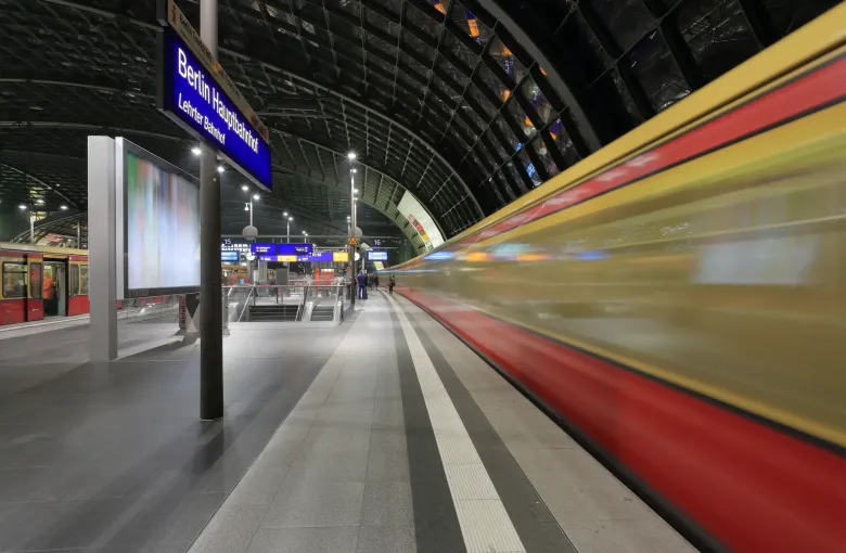 An S-Bahn train blurring through the upper platform at Berlin Hauptbahnhof beneath the station's name board.