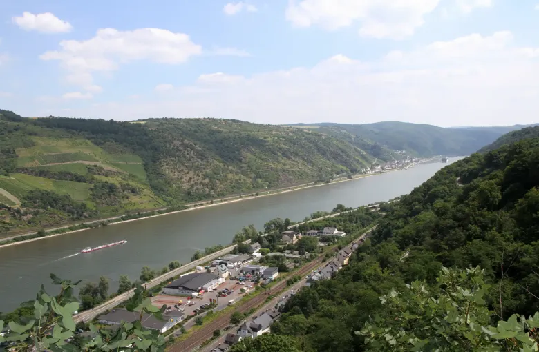 The Rhine curving between steep vineyard slopes near Oberwesel, with a barge on the water and a railway along the bank.