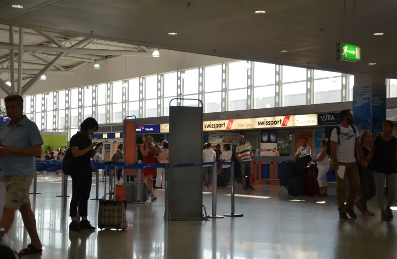 Travelers with baggage at ticket desks in the departures hall of Athens International Airport, Greece.