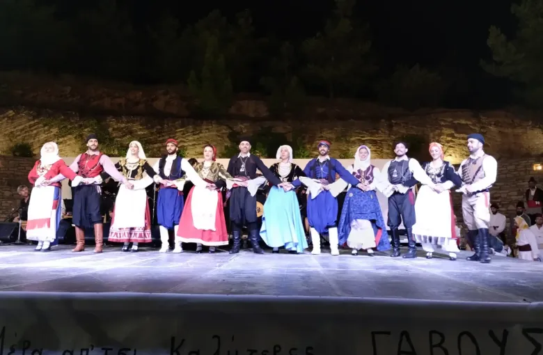 Dancers in Cretan costume holding hands in a line at an evening village festival in Crete, Greece.
