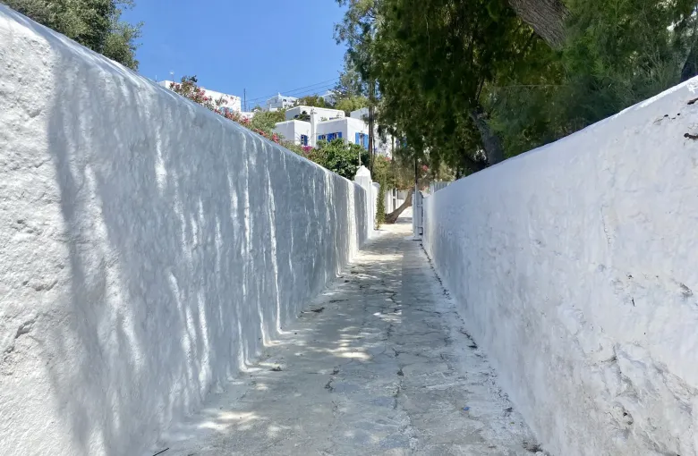 A narrow whitewashed lane with a worn stone surface running between high walls in Mykonos Chora, Greece.