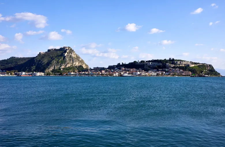 The old town of Nafplio along the water with the Palamidi fortress on the crag above, seen from the Argolic Gulf.