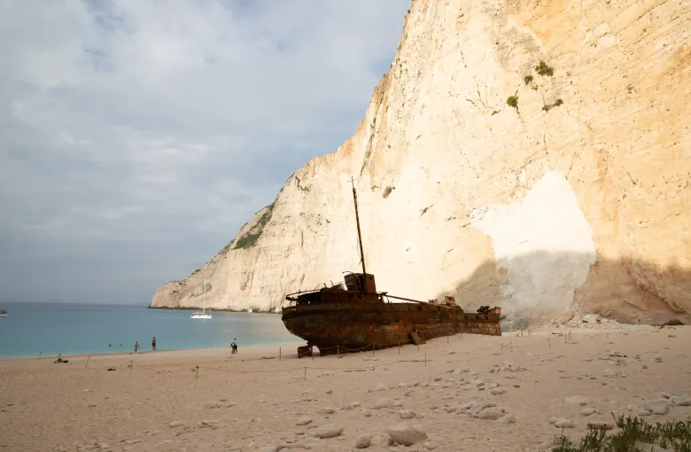 The rusted hull of the Panagiotis on the sand at Navagio beach below white limestone cliffs on Zakynthos, Greece.