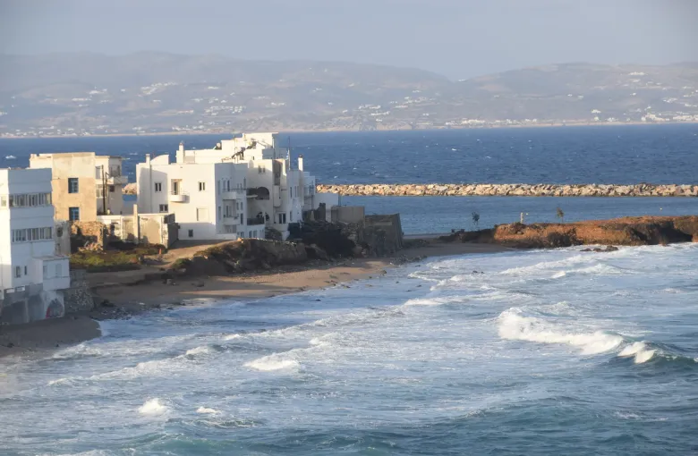 Whitewashed houses above a rough sea breaking along the waterfront at Naxos in the Cyclades, Greece, on a windy day.