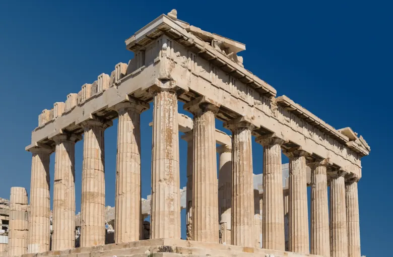 The Doric columns and pediment of the east front of the Parthenon on the Acropolis of Athens against a deep blue sky.