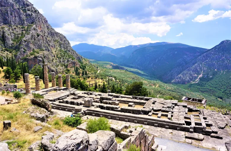 Standing columns of the Temple of Apollo above the terraced sanctuary at Delphi, with the olive valley and Parnassus beyond.