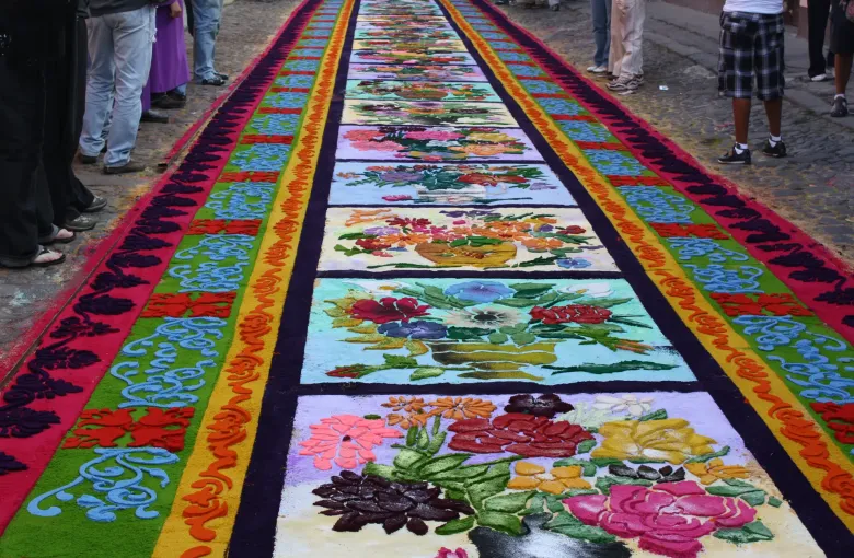 A carpet of dyed sawdust laid down the centre of a street in panels of flowers and geometric borders, ready for a Holy Week procession.