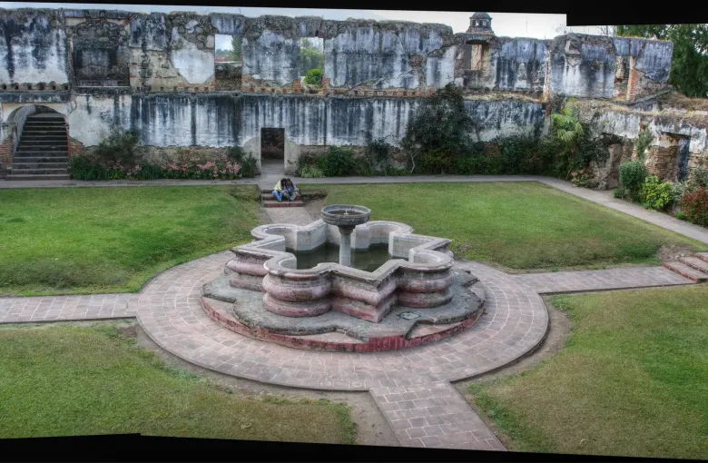 A fountain set in a lawned courtyard inside the roofless walls of an earthquake-ruined convent in Antigua.