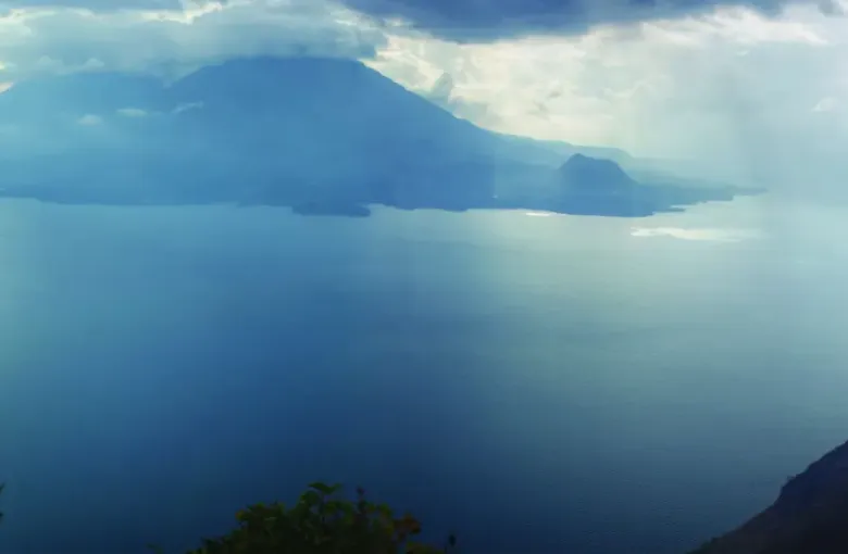 Shafts of light breaking through cloud over Lake Atitlan, with the volcanoes ranged along the far shore.