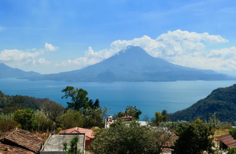 Lake Atitlan seen from a village above the shore, with three volcanoes standing across the water under high cloud.