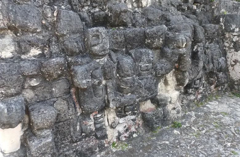 A row of weathered Maya mask carvings worked into the limestone facade of a temple platform at Tikal.