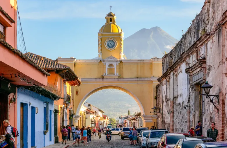 The yellow Santa Catalina Arch spanning a cobbled street in Antigua, with a volcano rising directly behind it.
