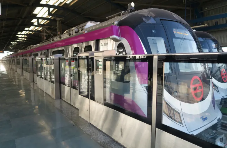 A Delhi Metro train standing at a platform behind full height platform screen doors.