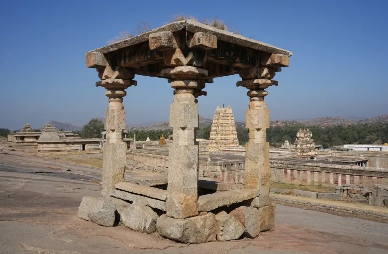 A stone pavilion on Hemakuta Hill at Hampi looking across the ruins to the Virupaksha temple tower.