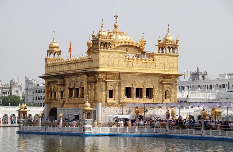 Harmandir Sahib standing in the sarovar at Amritsar with pilgrims on the causeway around it.