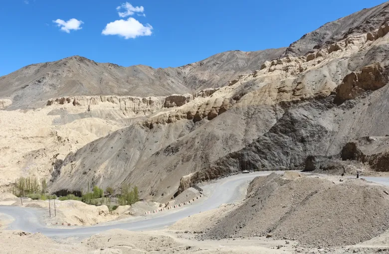 A road switching back through the bare eroded slopes of Ladakh, with painted markers along its edge.