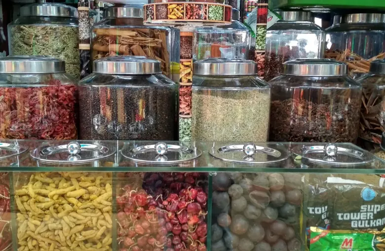 Glass jars of whole spices above open trays of dried chilies and tamarind at Palayam market in Kerala.