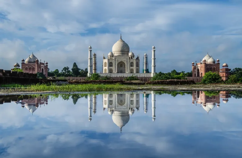 The Taj Mahal and its two flanking red sandstone buildings reflected in still water at Agra.
