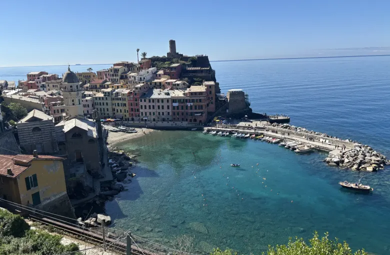Vernazza seen from above, its pastel houses and watchtower beside a turquoise harbor.
